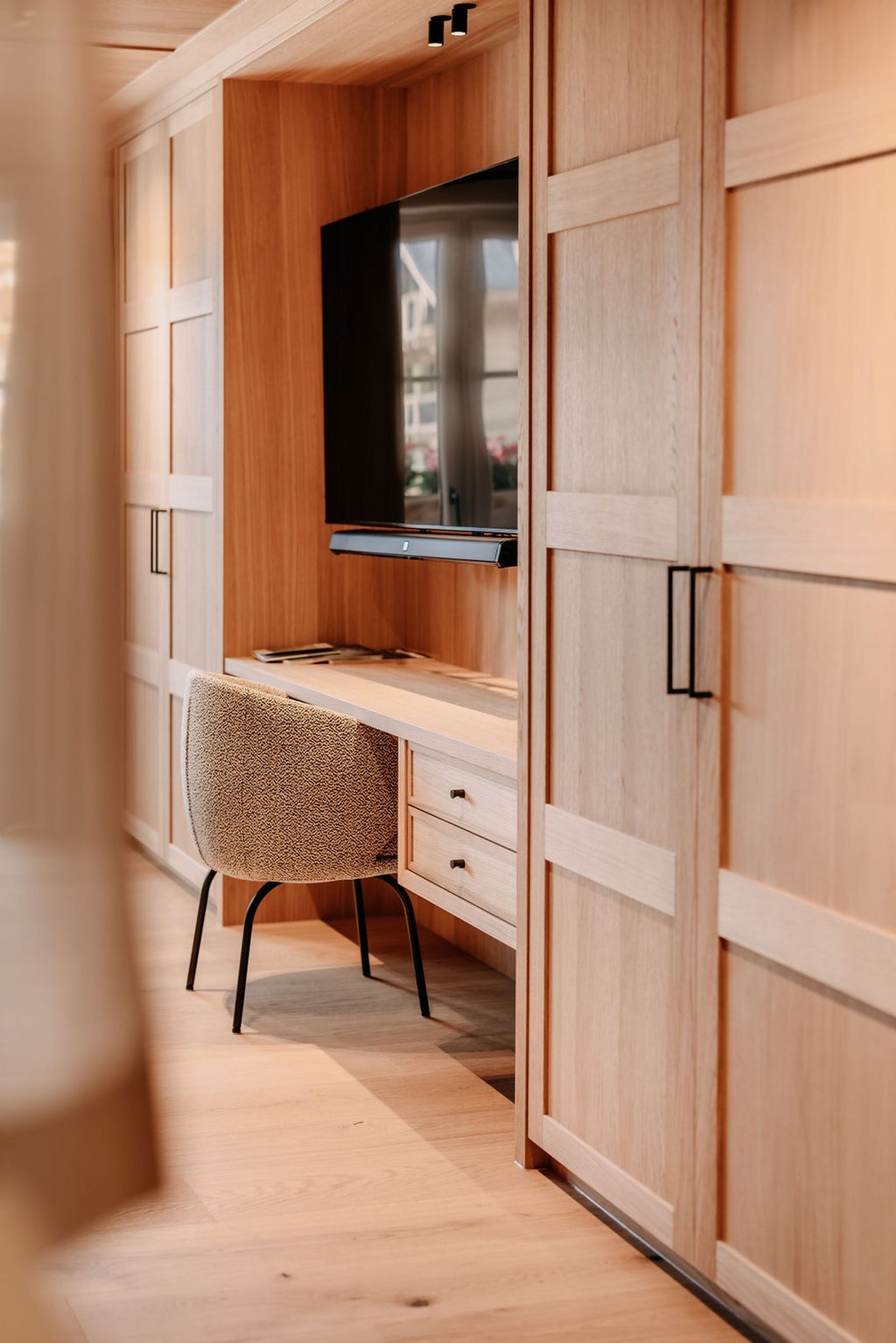 Stilvoll eingerichtetes Zimmer mit einem eleganten Holzschrank, einem Schreibtisch mit Stuhl und einem TV – warmes, natürliches Interior-Design für eine gemütliche Atmosphäre.