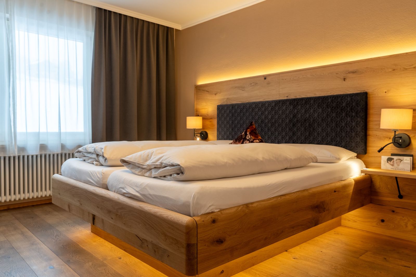 Doppelbett mit Fenster im Doppelzimmer Heimatglück im Biohotel Eggensberger mit Vorhängen und Nachttischlampen