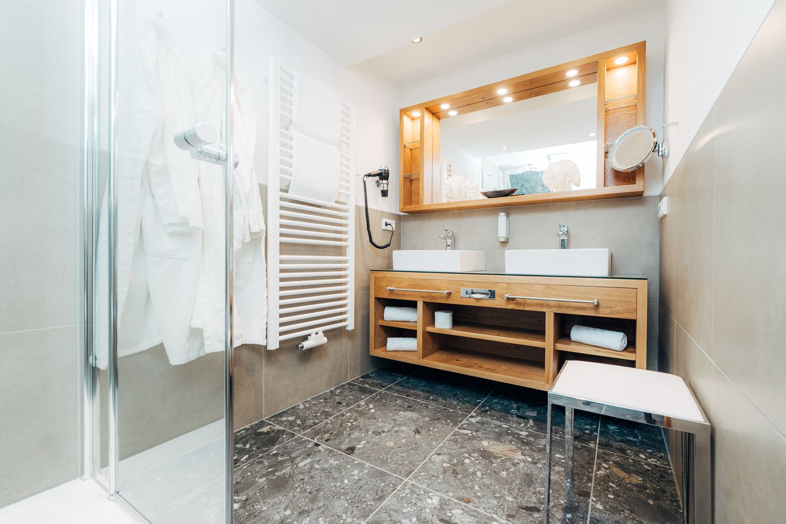 ein geräumiges Badezimmer mit bodentiefer Dusche und einem Waschtisch mit Doppelwaschbecken und großem Spiegel