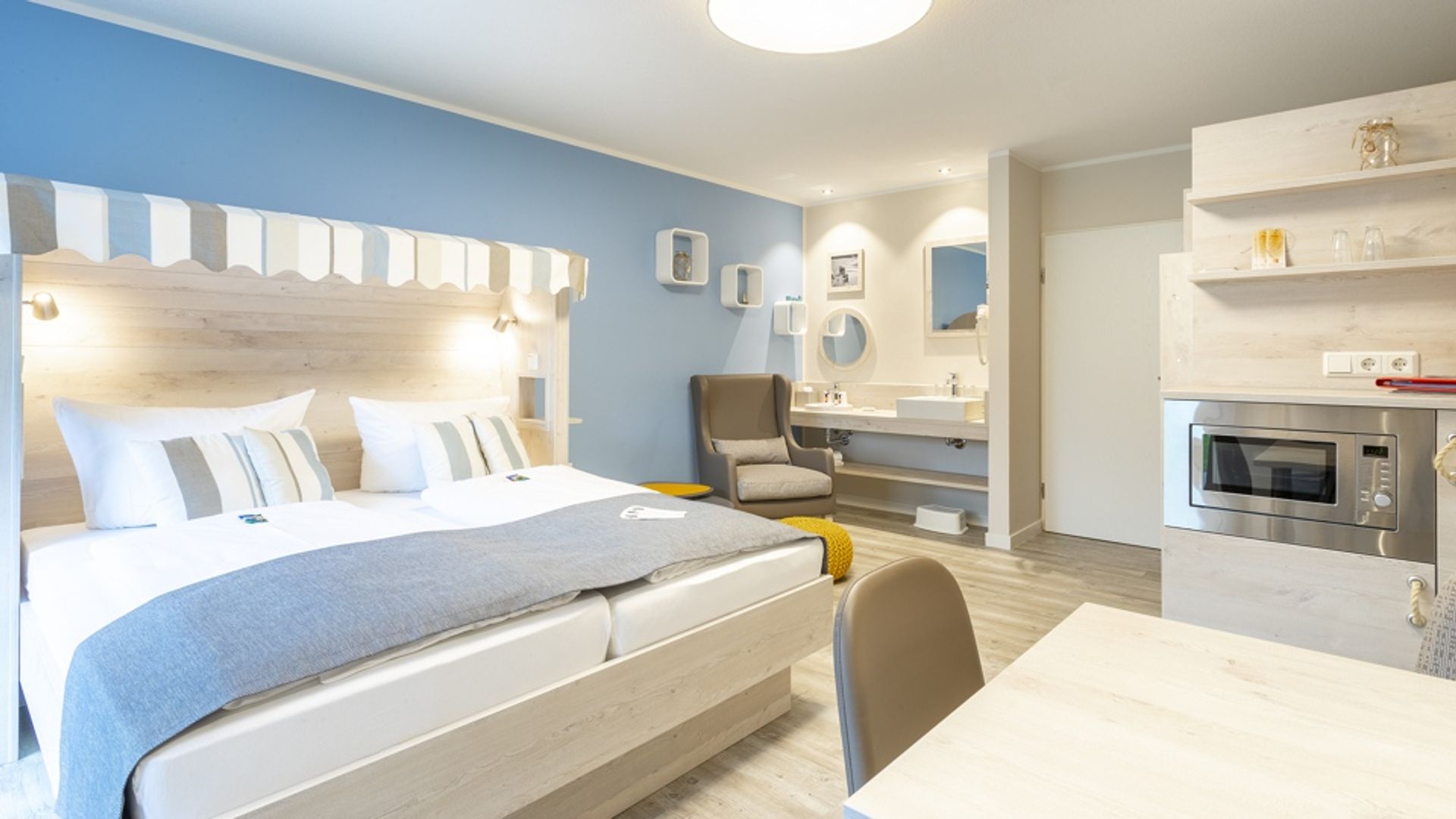 Links das Doppelbett mit Strandkorb-Stil, dahinter die Waschecke und rechts die Sitzecke und Schränke mit der Mikrowelle