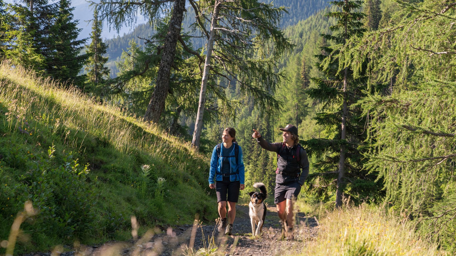 Zwei Wanderer mit Hund auf Waldweg in Gastein – Naturerlebnis und Aktivurlaub nahe Hotel Sonngastein.