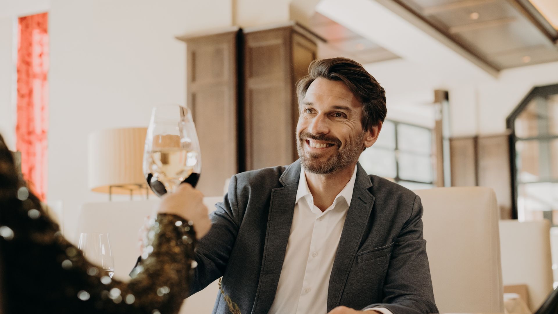 Mann beim Anstoßen mit Weißwein im Restaurant – Genuss und stilvolle Urlaubsmomente im Hotel Sonngastein.