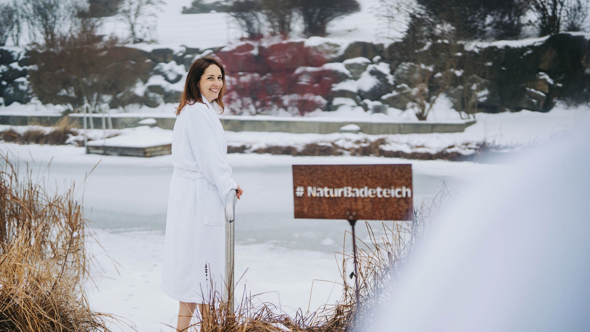Frau steht vom Naturbadeteich im Winter