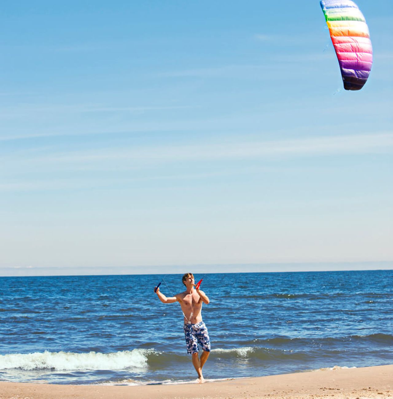 Foto von einem jungen Mann in Badehose, der bei seinem Strandurlaub in Heringsdorf einen bunten Drachen im Himmel lenkt