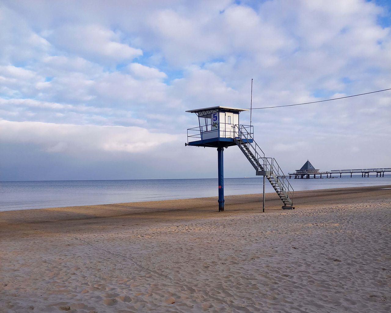 Aufnahme von einem Rettungsschwimmer-Turm bei blauem Himmel, der an einem menschenleeren Strand an der Ostsee steht