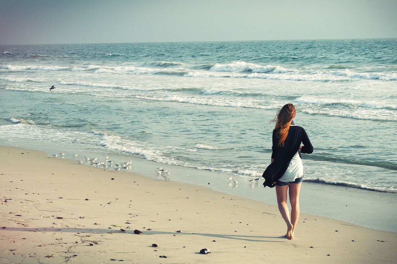 Eine junge Frau macht alleine Urlaub an der Ostsee und läuft am Strand entlang des Wassers, vor ihr sind viele Möwen zu sehen