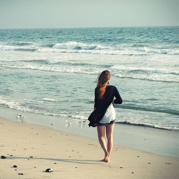 Eine junge Frau macht alleine Urlaub an der Ostsee und läuft am Strand entlang des Wassers, vor ihr sind viele Möwen zu sehen