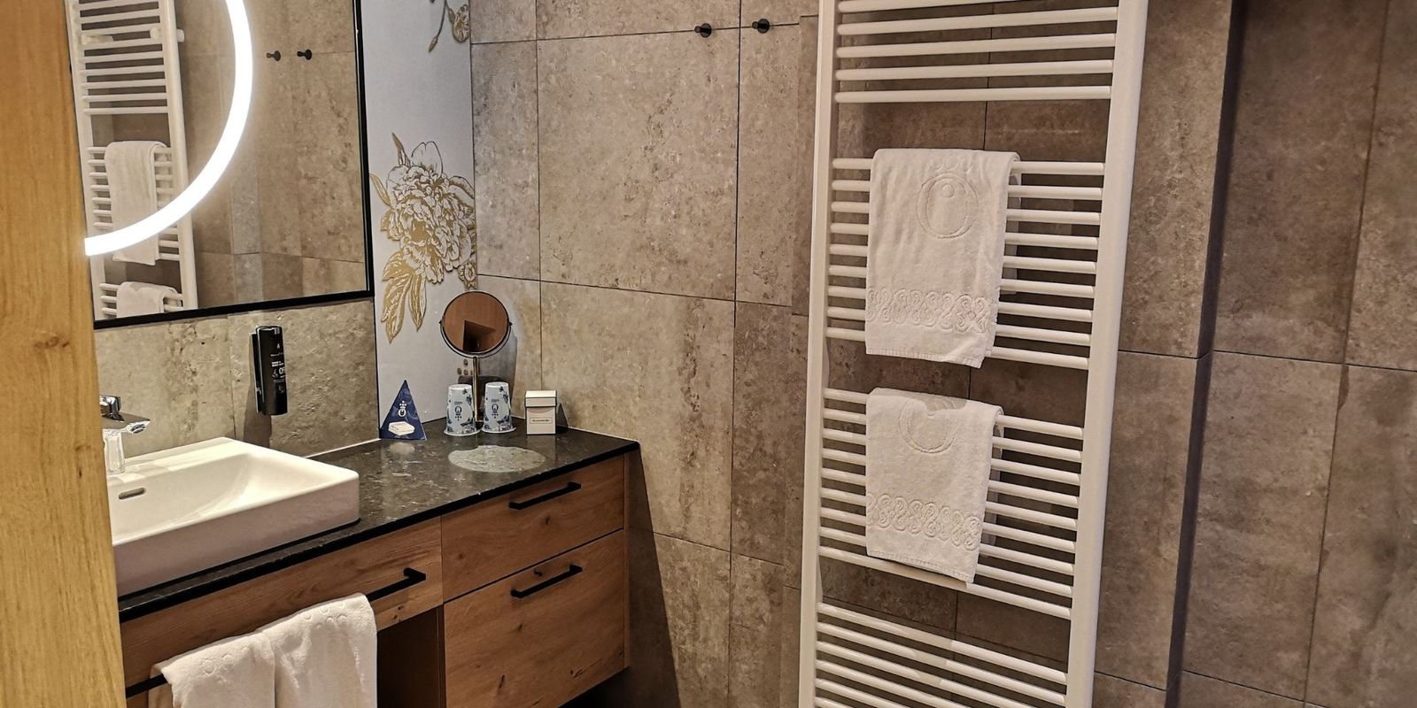 Das Badezimmer der HOCHKÖNIGIN verbindet natürliche Materialien mit modernem Design. Steinoptik, Holz und warme Beleuchtung schaffen ein stilvolles Ambiente für erholsame Momente in Maria Alm.