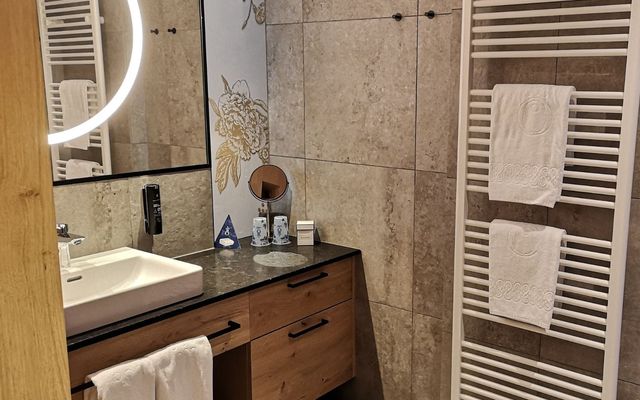 Das Badezimmer der HOCHKÖNIGIN verbindet natürliche Materialien mit modernem Design. Steinoptik, Holz und warme Beleuchtung schaffen ein stilvolles Ambiente für erholsame Momente in Maria Alm.