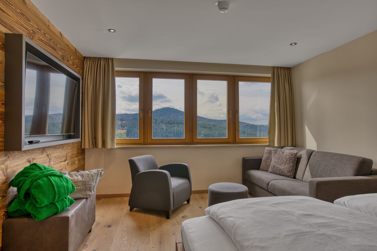 Schlafzimmer einer Suite mit Panoramafenster, Sofa und TV im Wellnesshotel Hofbräuhaus in Bodenmais, Bayerischer Wald